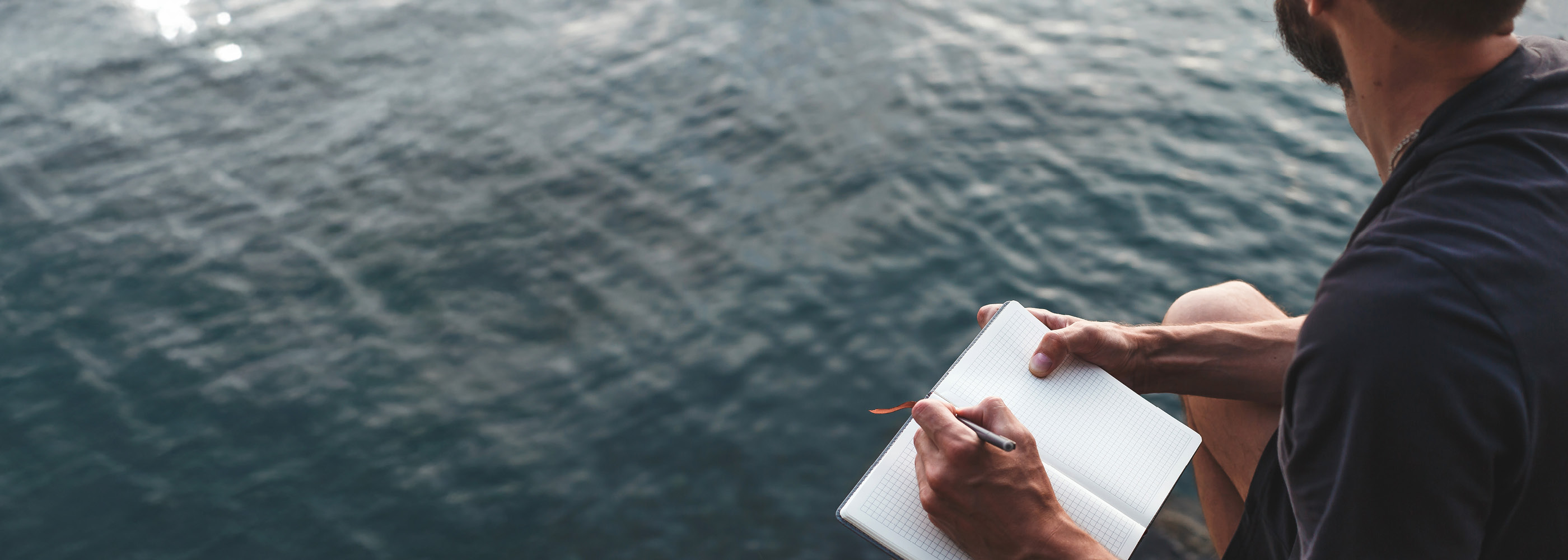 Un signore scrive su un taccuino e guarda il lago.